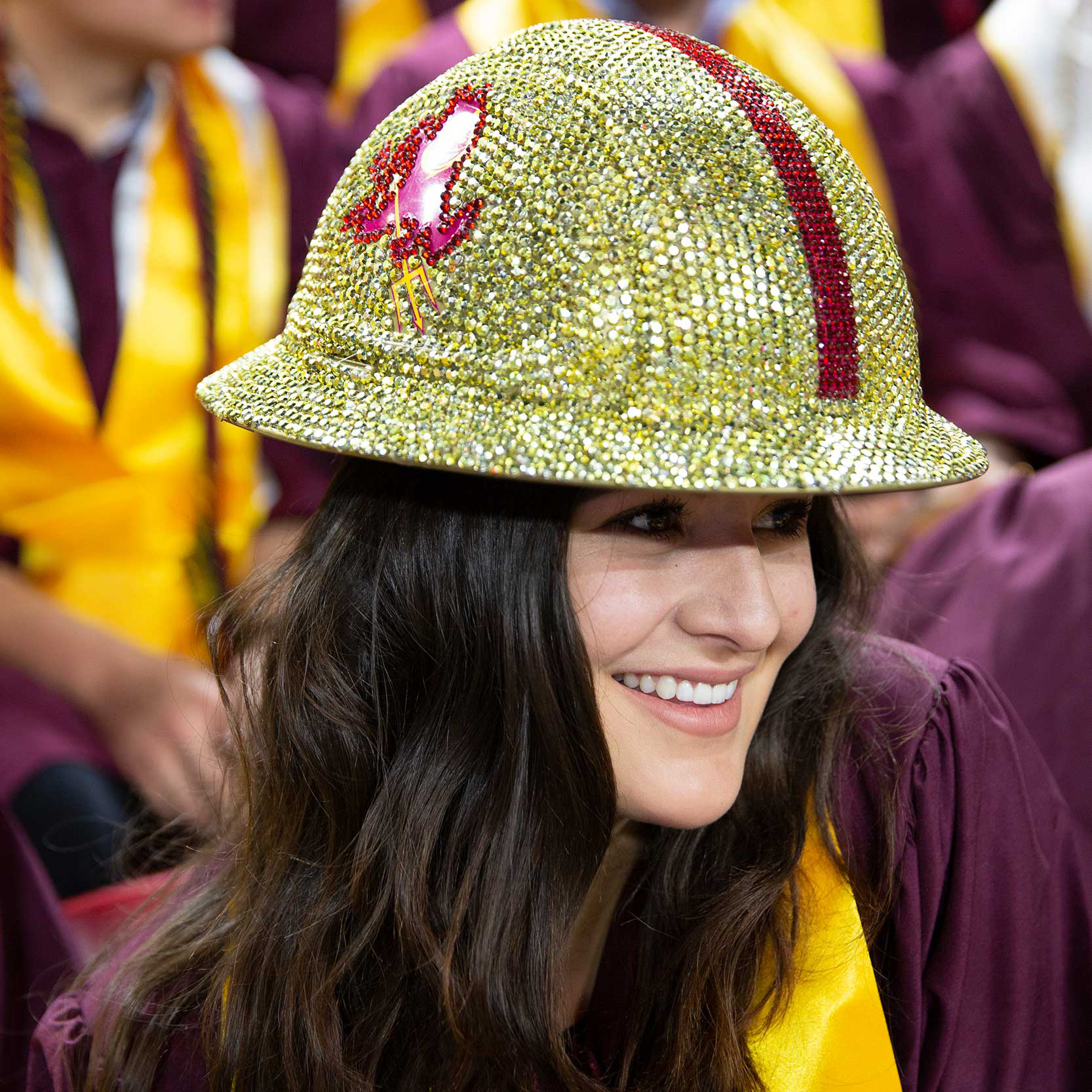 A construction graduate smiles as she shows off her bedazzled ASU hard hat