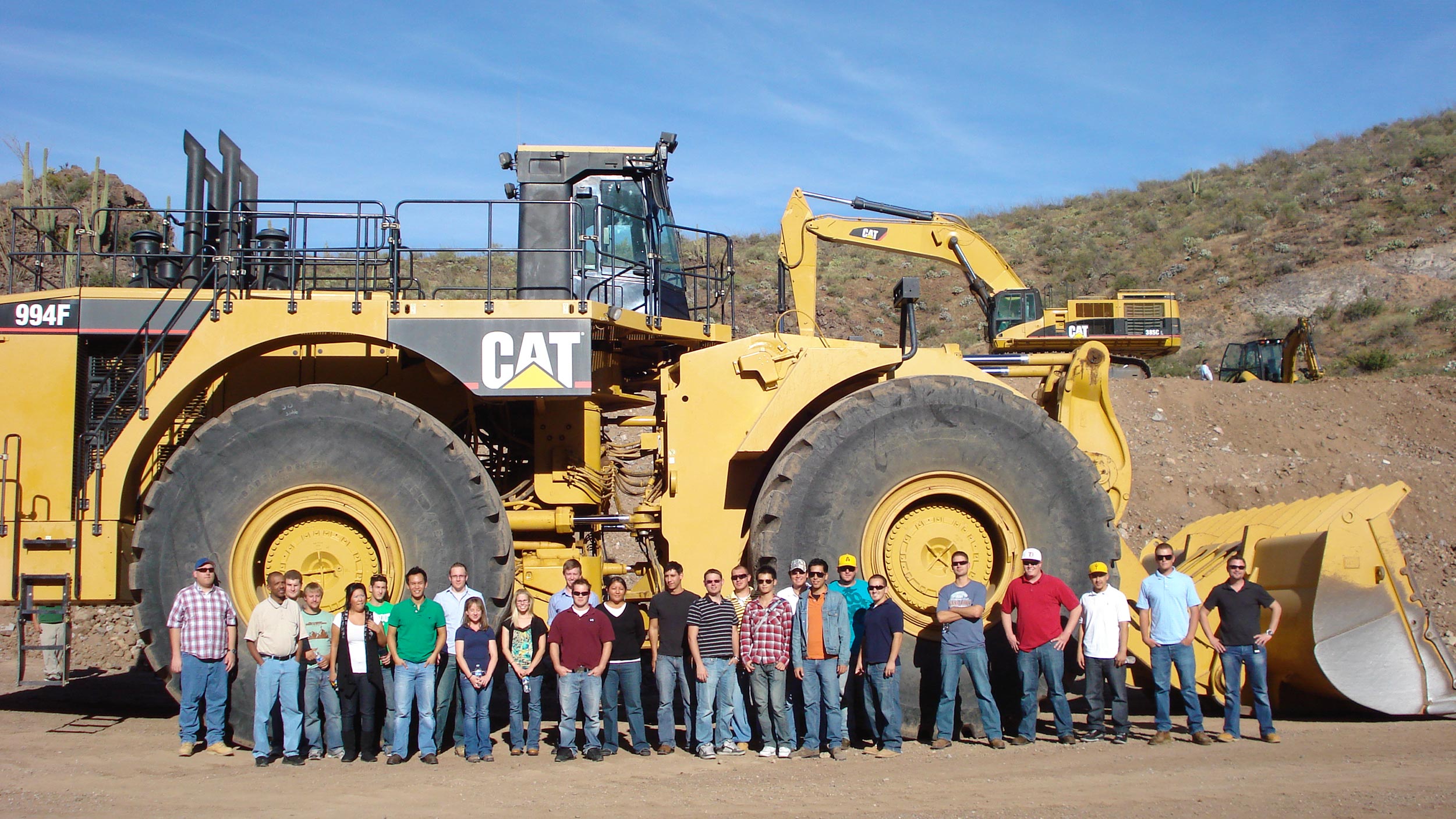 A group of students and construction professionals stand before an enormous CAT construction vehicle